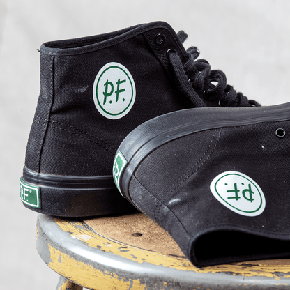 Black high-top sneakers with green P.F. Flyers logo resting on a rusty stool.