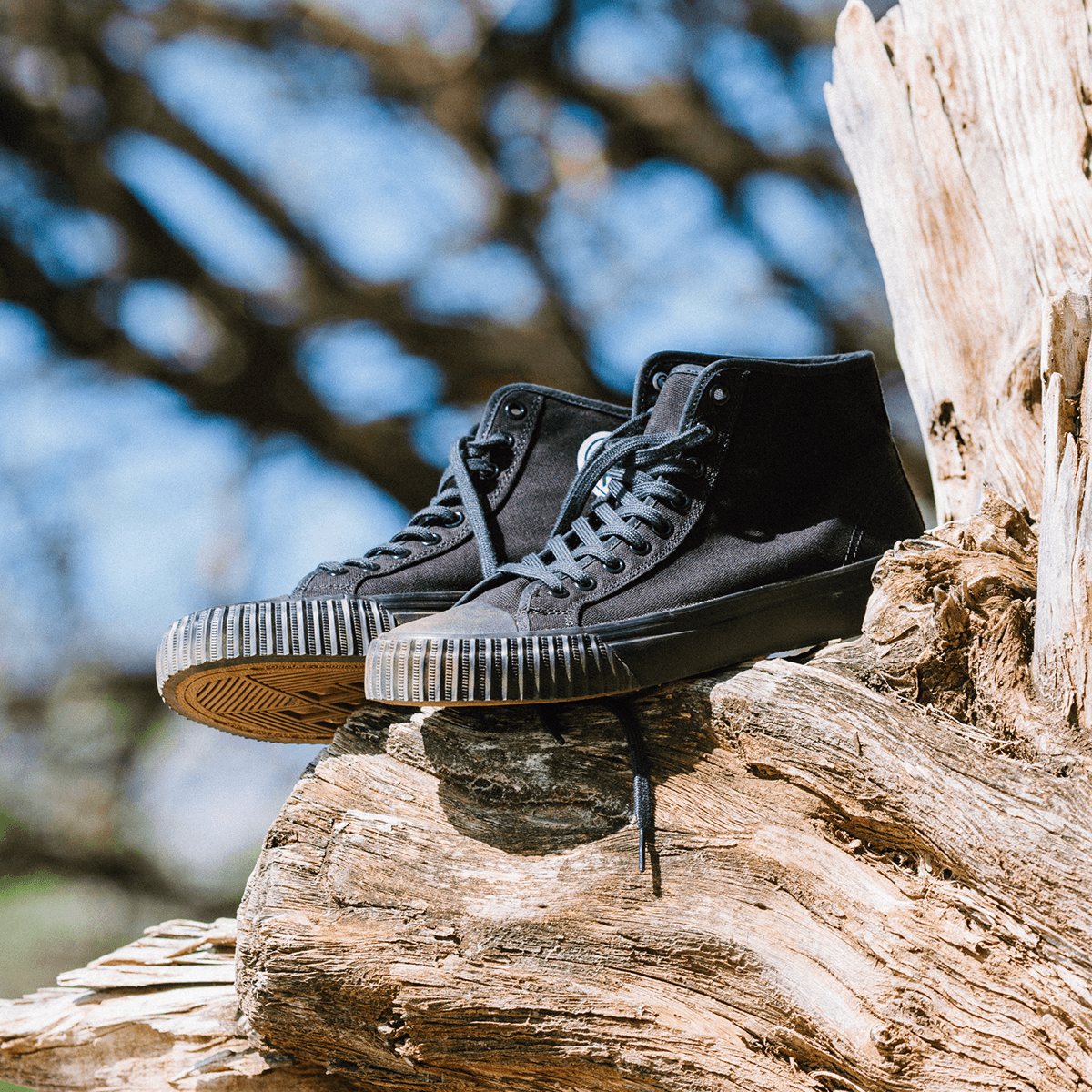 Black high-top sneakers on a wooden log outdoors.