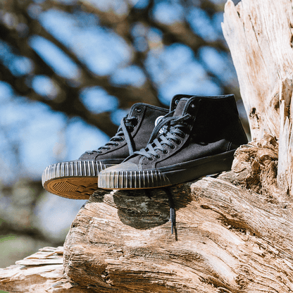Black high-top sneakers on a wooden log outdoors.