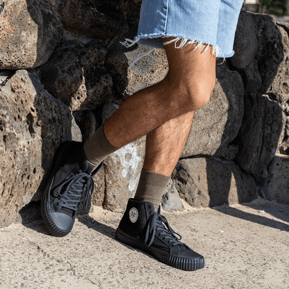 Person wearing black high-top sneakers and light denim shorts standing against a stone wall.