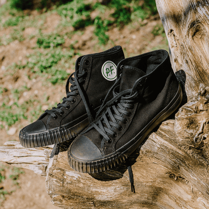 Black high-top sneakers on a wooden log outdoors.
