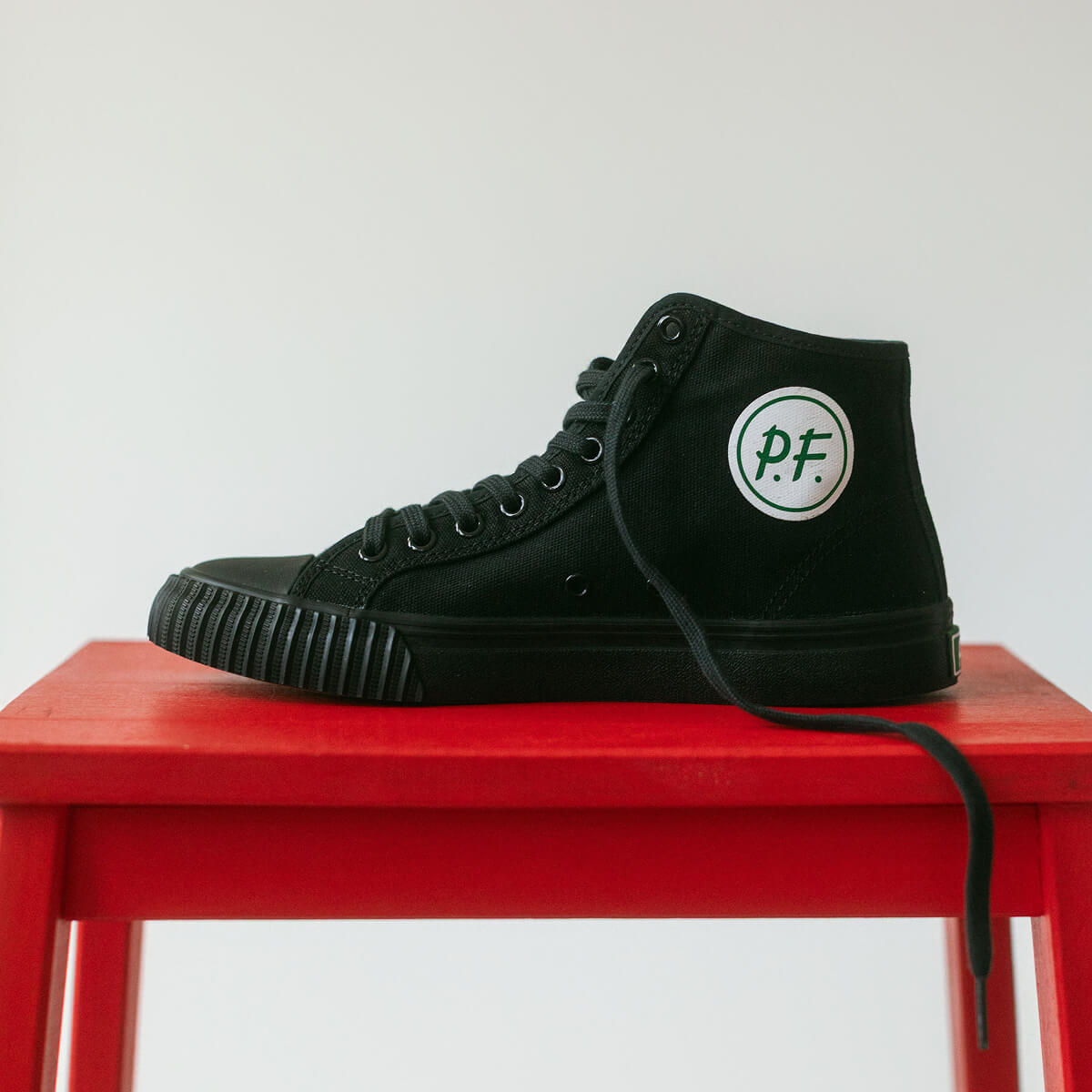 Black high-top sneaker with the P.F. Flyers logo on a red stool against a white background