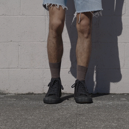 Person wearing black high-top sneakers and light denim shorts shifting stance against a stone wall.