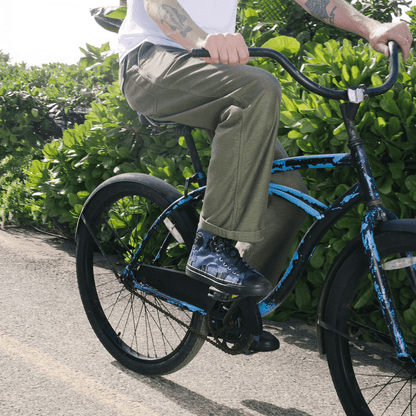 Person riding a blue bicycle on a paved path with greenery in the background