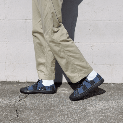 Person wearing beige pants and navy checkered shoes against a gray wall.