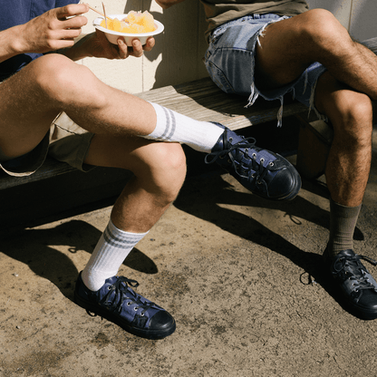 Two people sitting on a bench wearing sneakers and shorts, one holding a bowl of fruit.