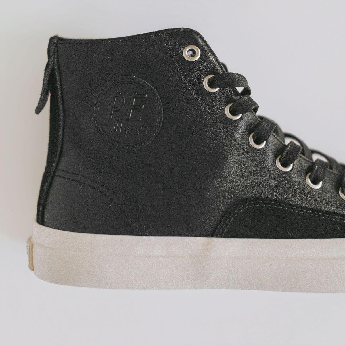 Black leather high-top sneaker with a visible P.F. Flyers logo on a light gray background