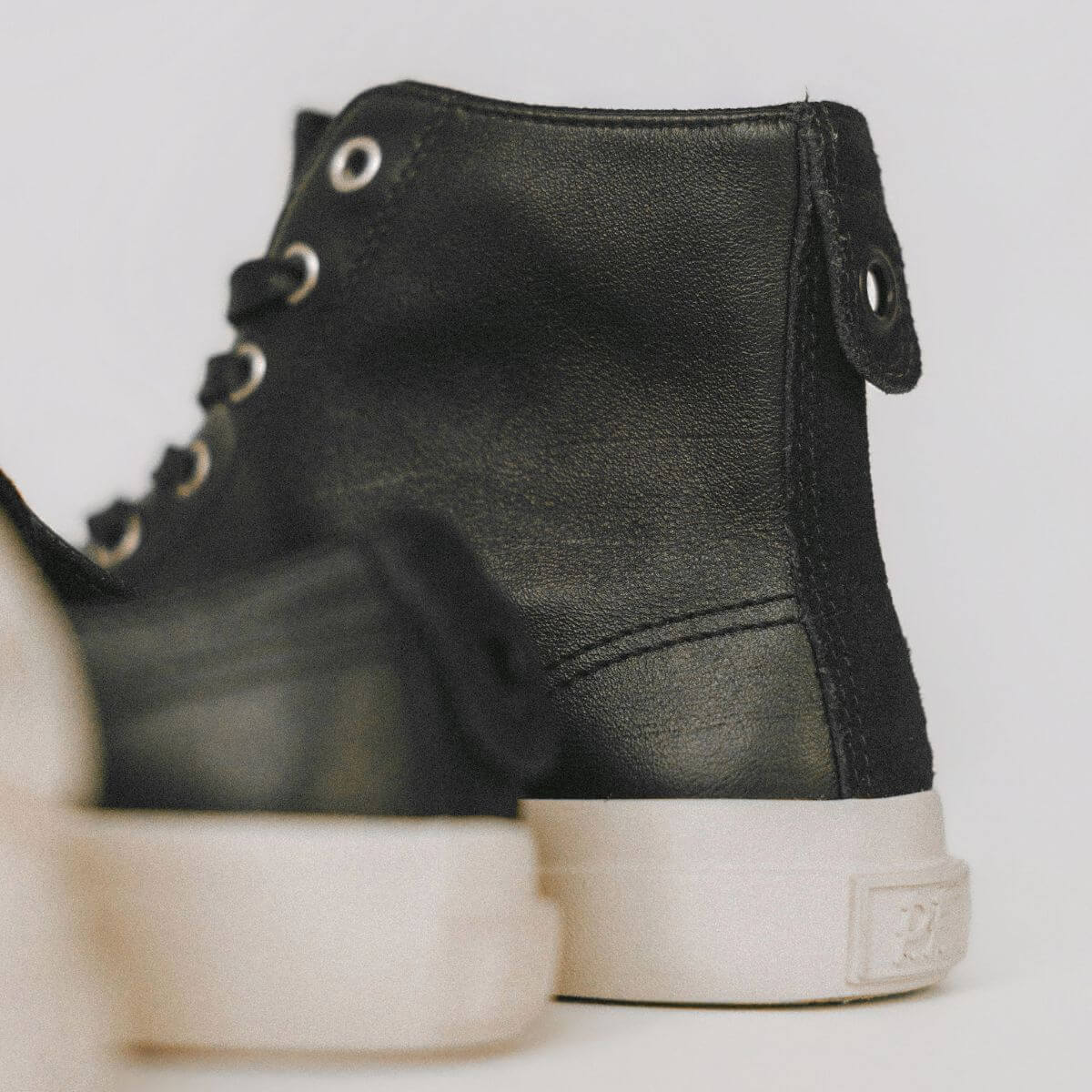 Black leather high-top sneakers with white soles on a light background