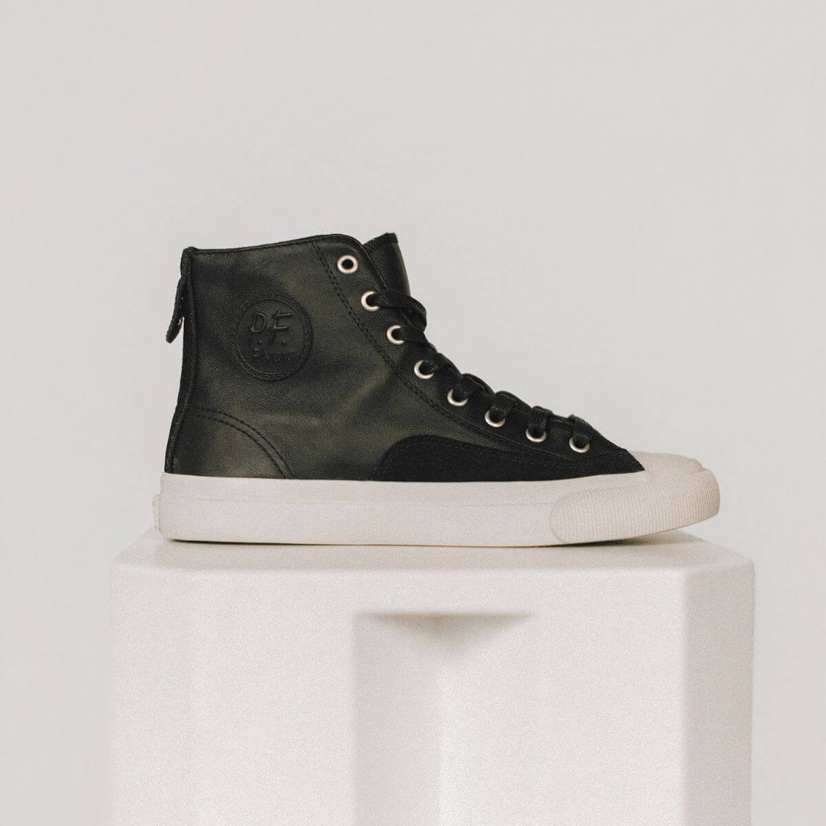 Black leather high-top sneaker with white sole on a light gray background