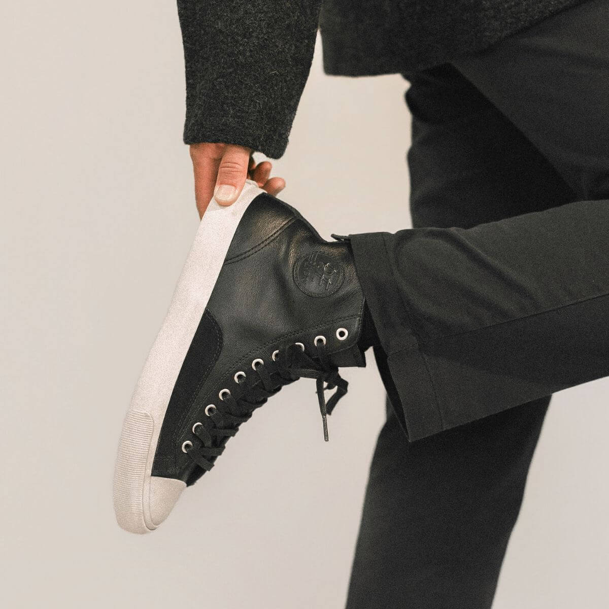 Person wearing black leather high-top sneakers with white soles on a plain background