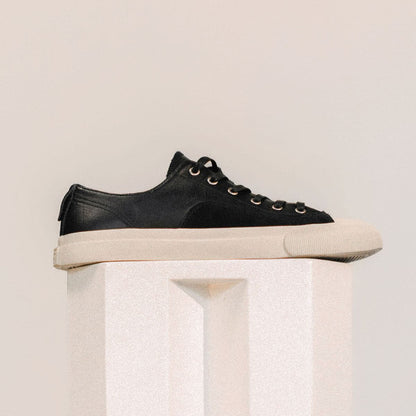 Black sneaker with white sole on a light beige pedestal against a light beige background
