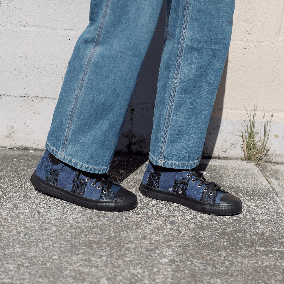 Person wearing blue jeans and navy high-top sneakers with black soles on a sidewalk.