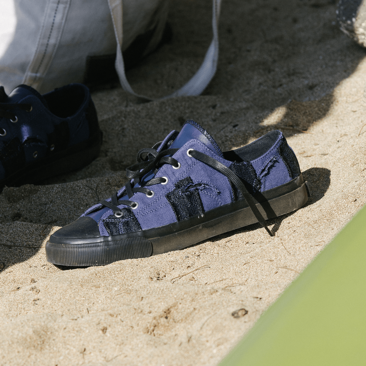 Navy low-top sneakers with black soles on a sandy surface.