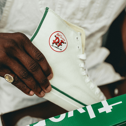 Close up of person holding a white high-top sneaker with green accents.