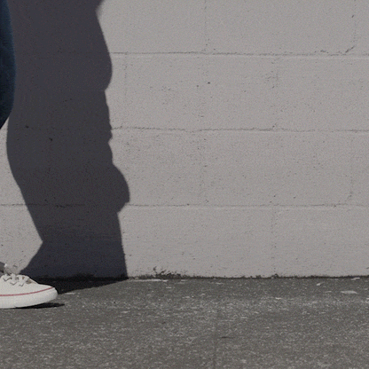 Person wearing white low-top sneakers and blue jeans shifting stance against a stone wall.