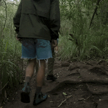 Man hiking a muddy trail wearing green denim high-top sneakers with black accents.