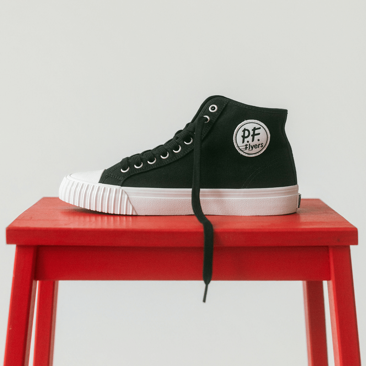 Black high-top sneaker with a white sole displayed on a red stool against a light background.