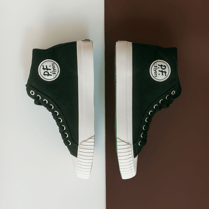 Black high-top sneakers with white soles on a white and brown background.