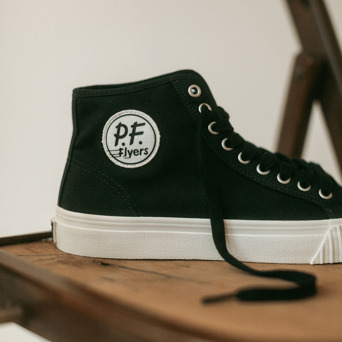 Close up of a black high-top sneaker with white soles on a wooden chair.