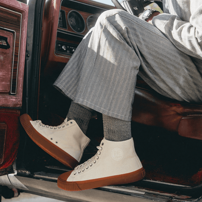 Person wearing white high-top sneakers with brown soles sitting inside a vehicle.