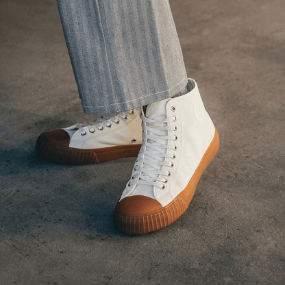 White high-top sneakers with brown soles worn by a person on a concrete floor.