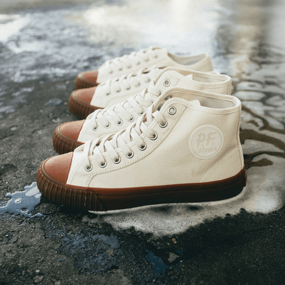 Two pairs of white sneakers with brown soles on a wet pavement.