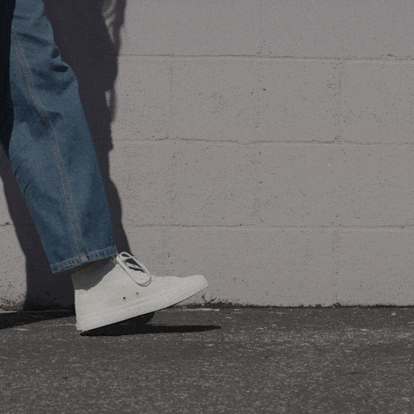 Person wearing white high-top sneakers and blue jeans shifting stance against a stone wall.