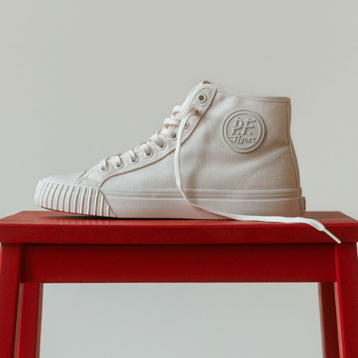 White high-top sneaker with P.F. Flyers logo on a red stool against a light gray background.