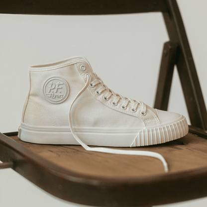 White high-top sneaker with a P.F. Flyers logo on a metal chair.