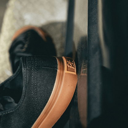 Close-up of a black low-top sneaker with a brown sole on a blurred background.