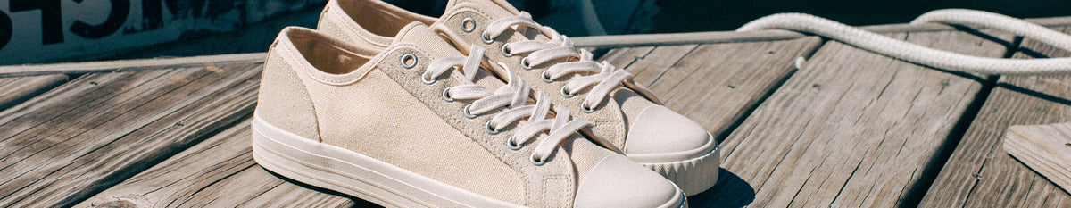 A pair of beige low-top sneakers resting on a wooden dock.