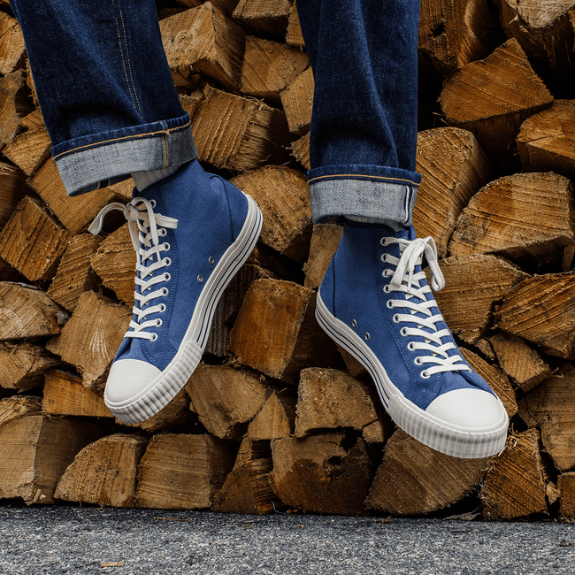 Person wearing blue high-top sneakers with white soles while sitting on a pile of firewood.
