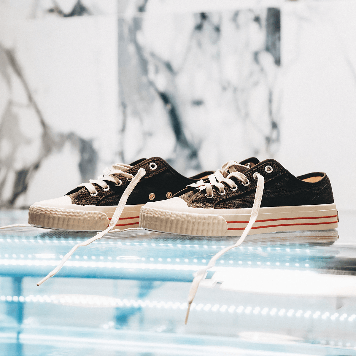 Pair of black low-top sneakers with white soles on a reflective surface.