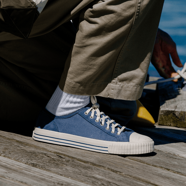 Person wearing blue low-top sneakers with white soles on a wooden surface.