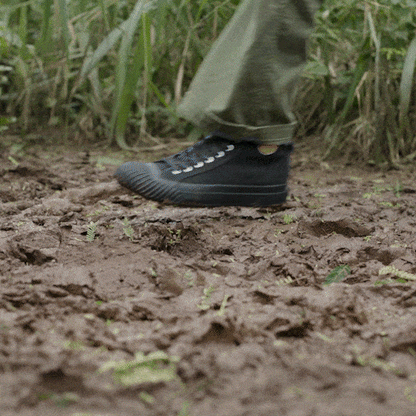 Person wearing black high-top sneakers and green pants on a muddy hiking trail.