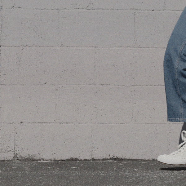 Person wearing white high-top sneakers and blue jeans shifting stance against a stone wall.