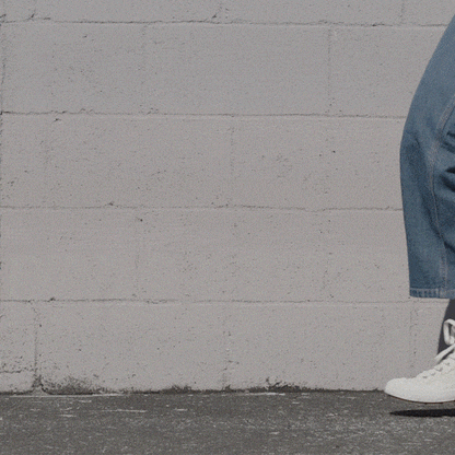 Person wearing white high-top sneakers and blue jeans shifting stance against a stone wall.