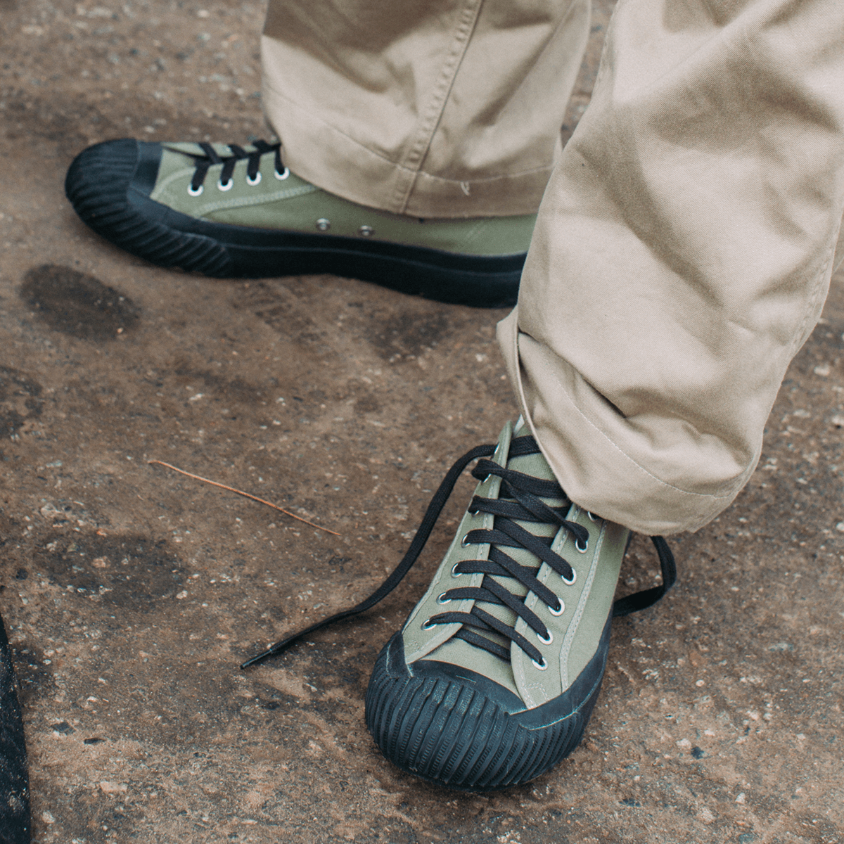 Olive green sneakers with black soles worn by a person on a concrete surface.