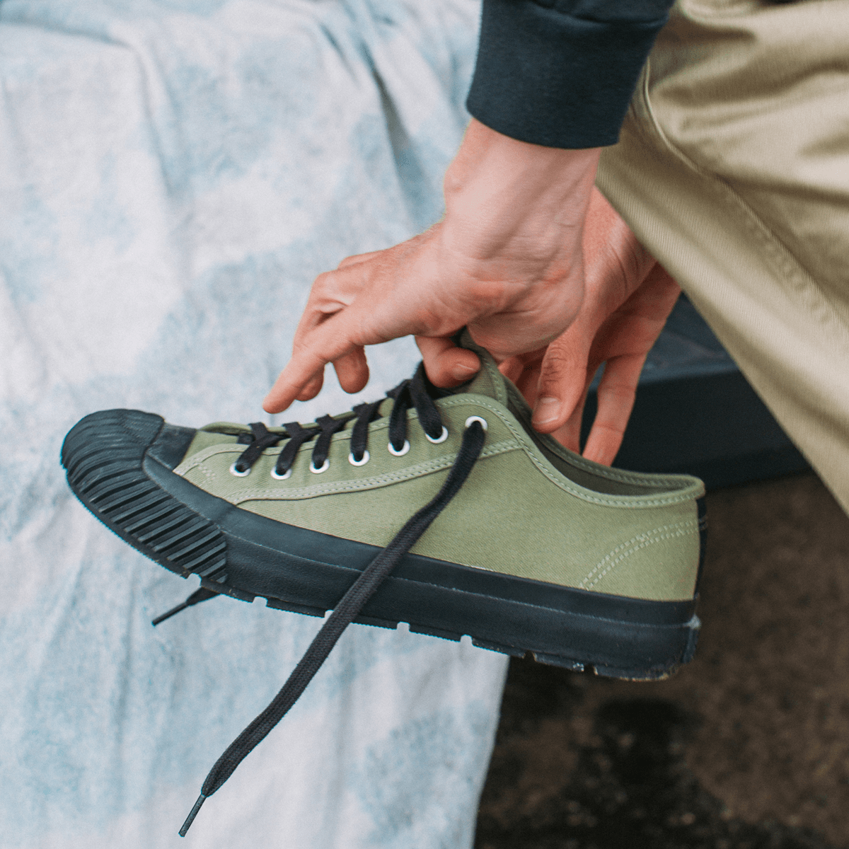 Person holding an olive green sneaker with a black sole.