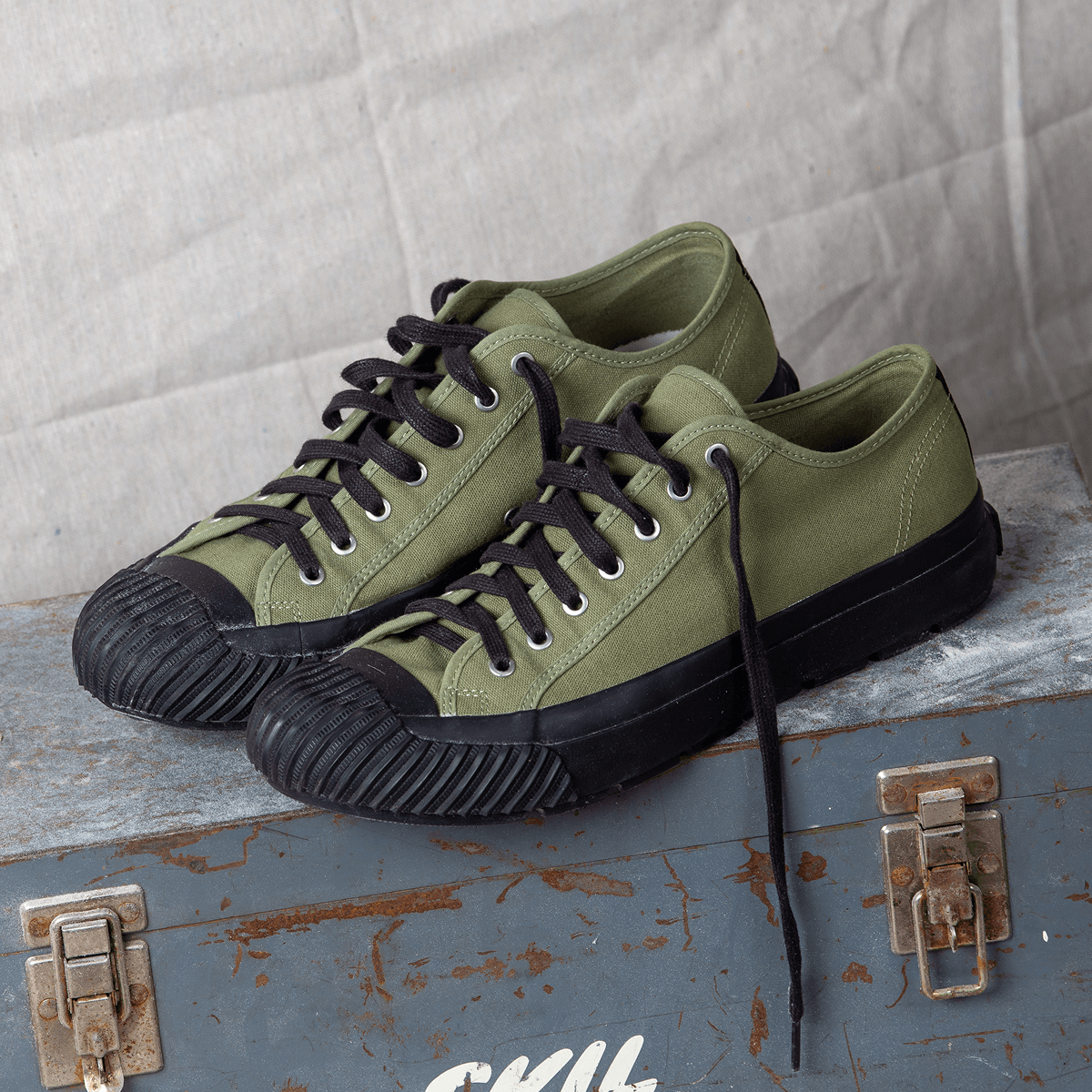 Olive green low-top sneakers with black soles on a metal container.
