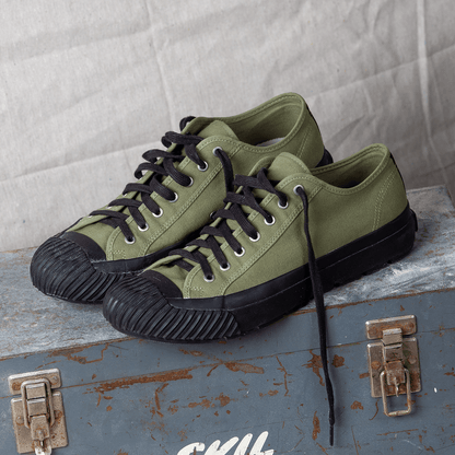 Olive green low-top sneakers with black soles on a metal container.