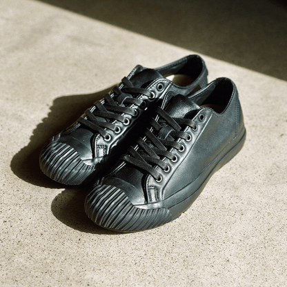 Pair of black leather low-top sneakers on a concrete floor.