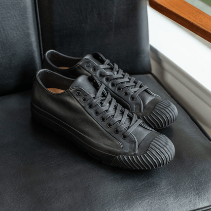 Black leather low-top sneakers on a chair.