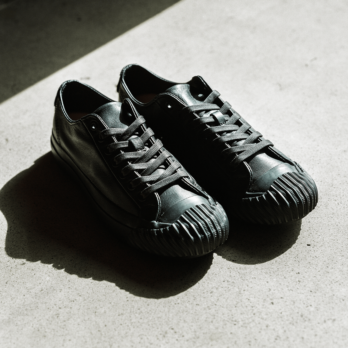 Pair of black leather low-top sneakers on a concrete floor.