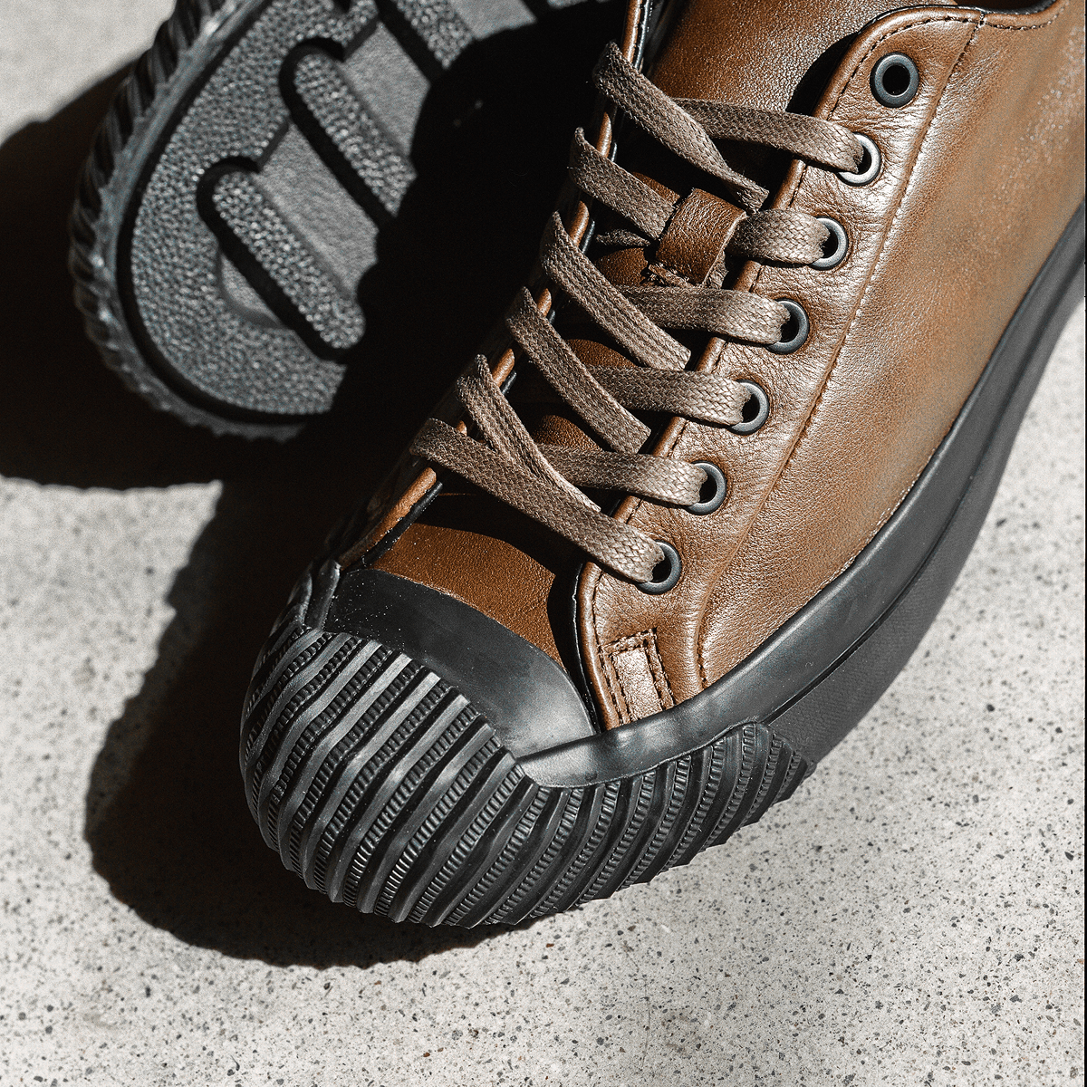 Close up of brown leather low-top sneakers with black soles on a concrete floor.