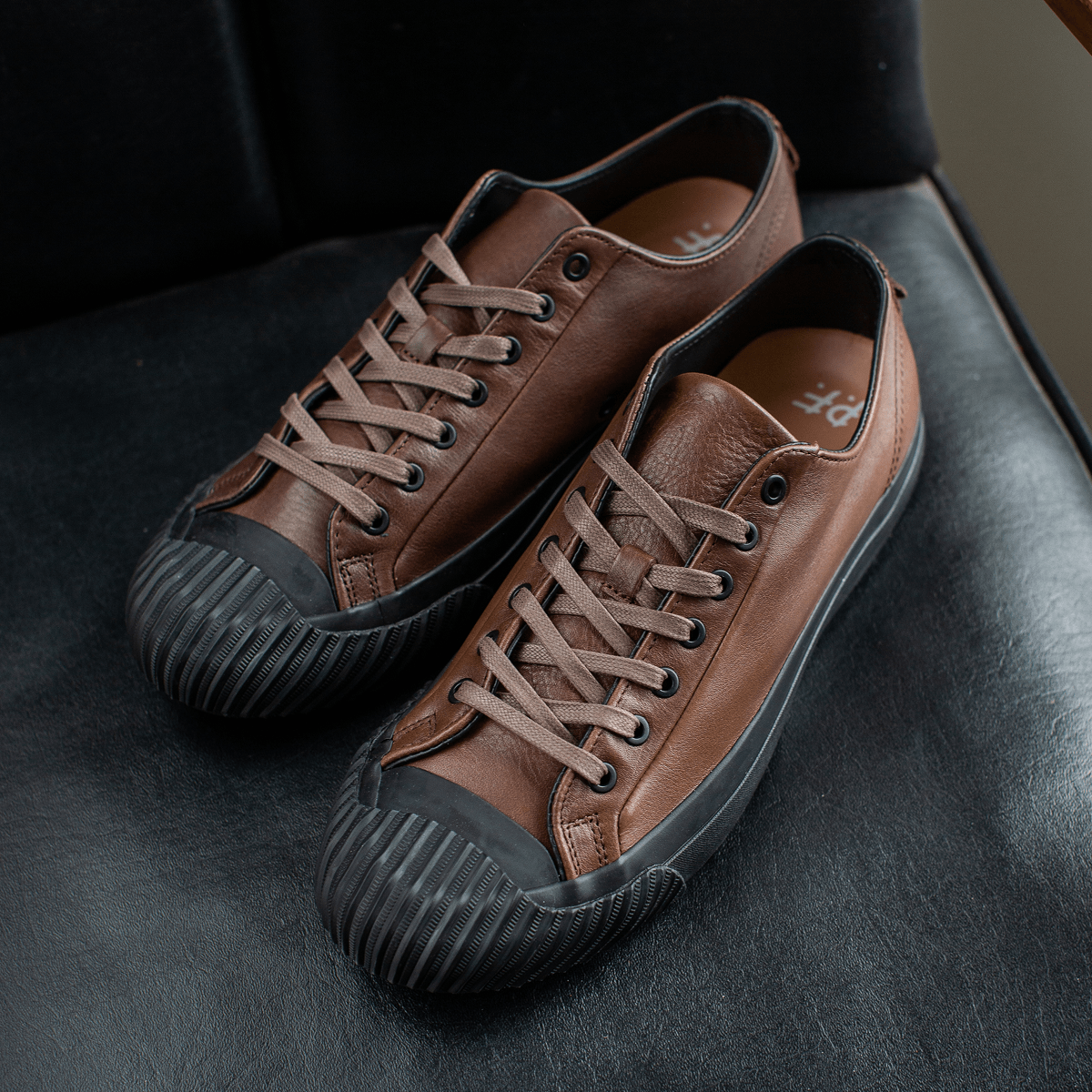 Brown leather low-top sneakers on a chair.