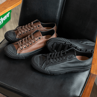 Pair of brown and black leather low-top sneakers on a black chair.