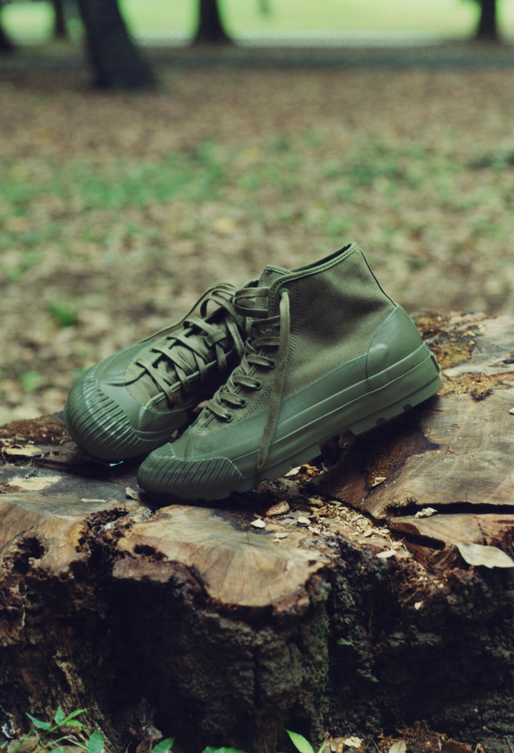 A pair of olive green canvas boots resting on a tree stump with a blurred forest background.