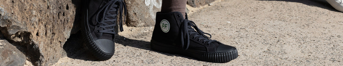 Close-up of a person wearing black high-top sneakers on concrete.