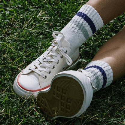 Close-up of white low-top sneakers with crimson accents, worn with white ankle socks on grass.